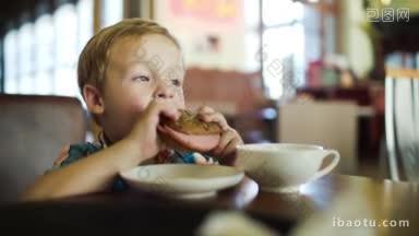 一个小男孩独自坐在咖啡馆里吃三明治